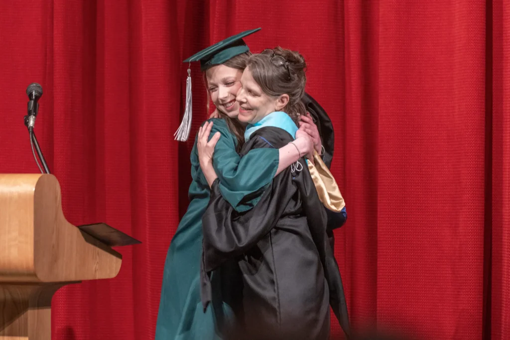 Graduate and teacher in cap and gowns hugging on stage